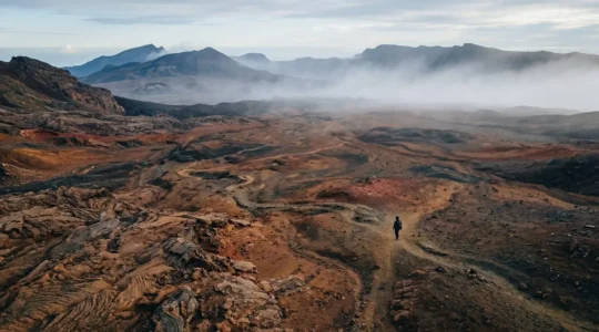 Paysage volcanique rouge et noir de la Plaine des Sables avec un randonneur solitaire au loin, entre brume matinale et ciel bleu