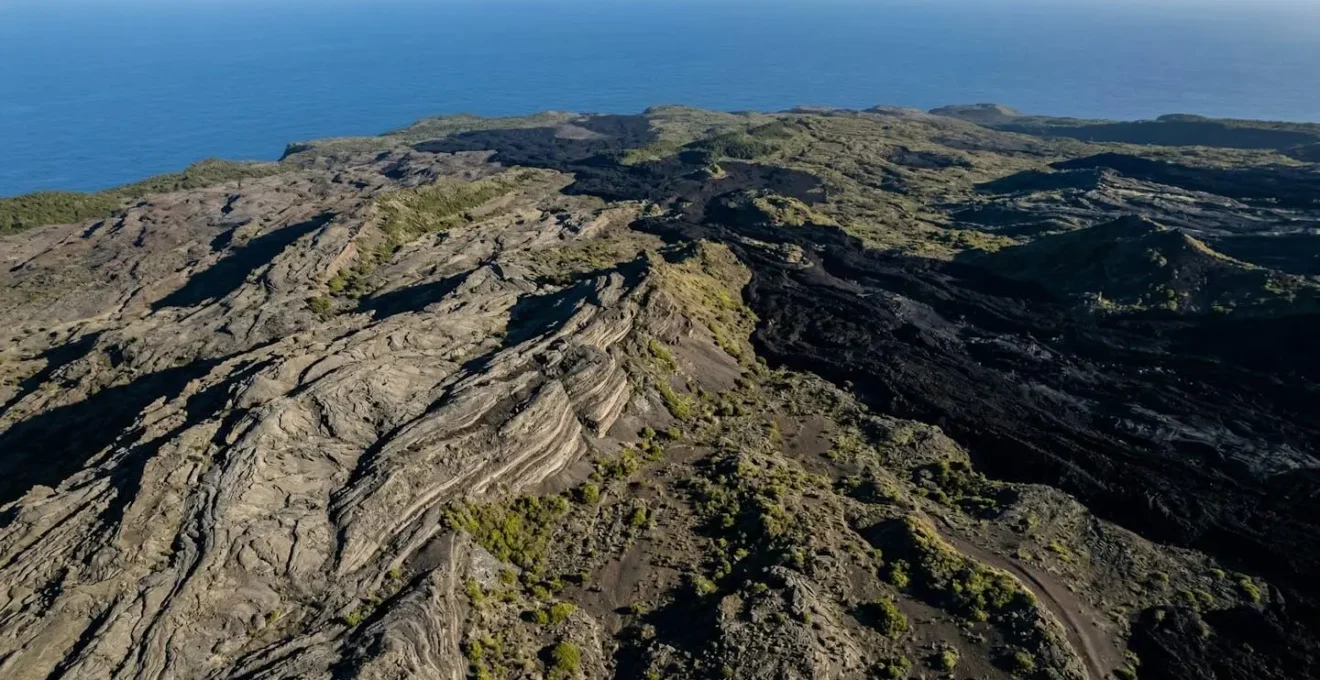 Vue aérienne spectaculaire des flancs du Piton de la Fournaise avec ses coulées de lave solidifiées formant un paysage lunaire de roches volcaniques superposées