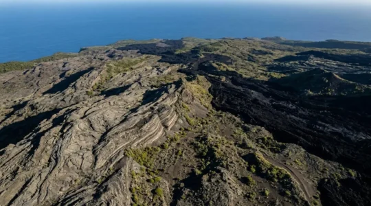 Vue aérienne spectaculaire des flancs du Piton de la Fournaise avec ses coulées de lave solidifiées formant un paysage lunaire de roches volcaniques superposées