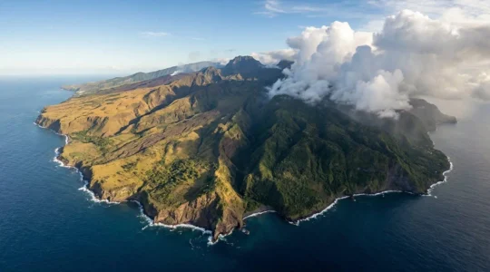 Vue aérienne spectaculaire de La Réunion montrant le contraste saisissant entre la côte Est verdoyante sous les nuages et la côte Ouest baignée de soleil