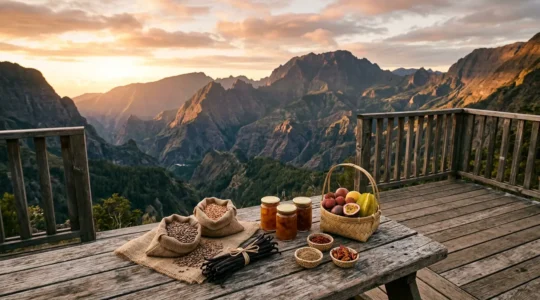 Vue panoramique d'une terrasse en bois avec des produits du terroir de La Réunion disposés sur une table rustique, le cirque de Cilaos en arrière-plan au coucher du soleil
